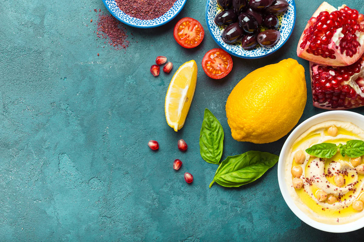 Assorted fruits, vegetables, and a bowl of hummus on a teal surface